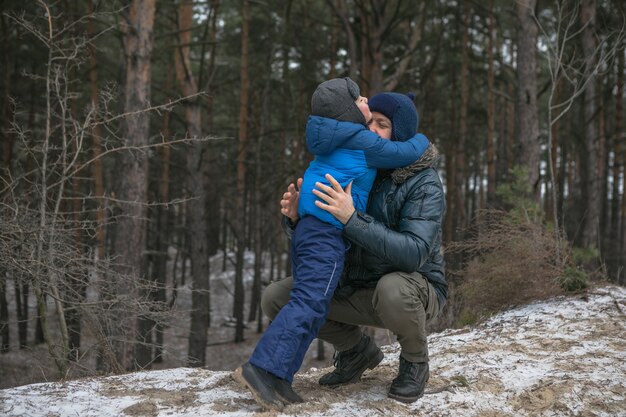 Happy family on a walk outdoors in sunny winter forest, Christmas holidays, father and son play together