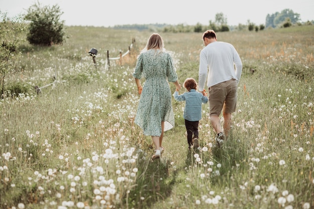 happy family walking in field of blooming flowers from behind, dad mom and son