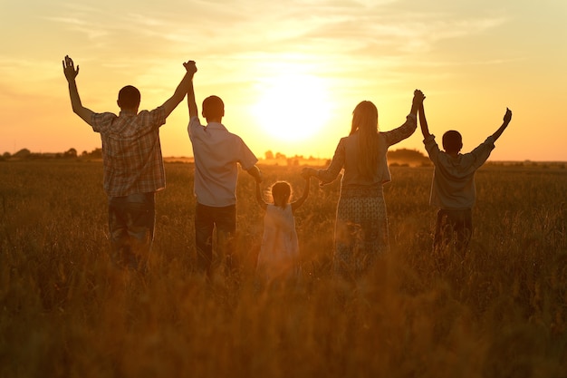 Famiglia felice che cammina nel campo al tramonto e si tiene per mano