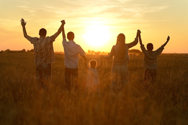 Фото Счастливая семья гуляет в поле на закате и держится за руки