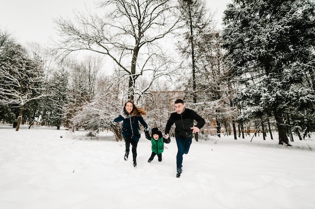 Happy family walking, playing in a snow winter park. Mom, dad throws up son. Emotions of happiness.