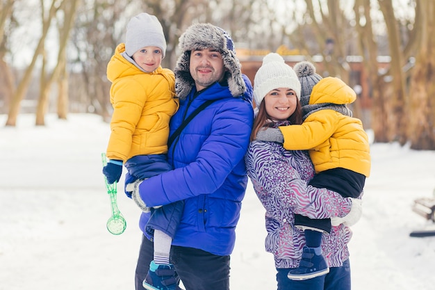 Happy family walking in winter park together, two adult man and woman and two children