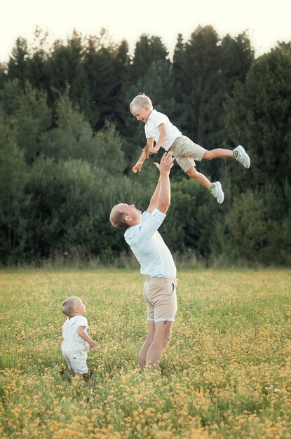 La famiglia felice cammina nel campo nel divertimento estivo al tramonto