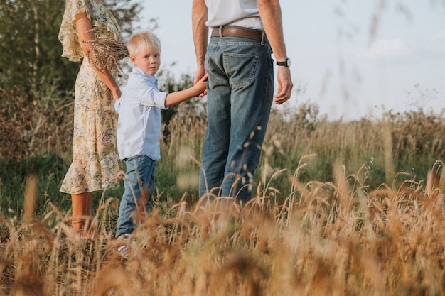 a happy family walks through a wheat field The parents hold their sons hands