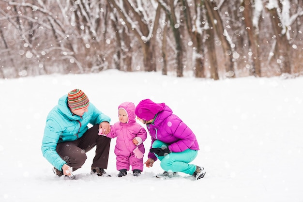 Счастливая семья гуляет в зимнем парке. Отец и мать с дочерью в тепловой одежде гуляют в холодный зимний день