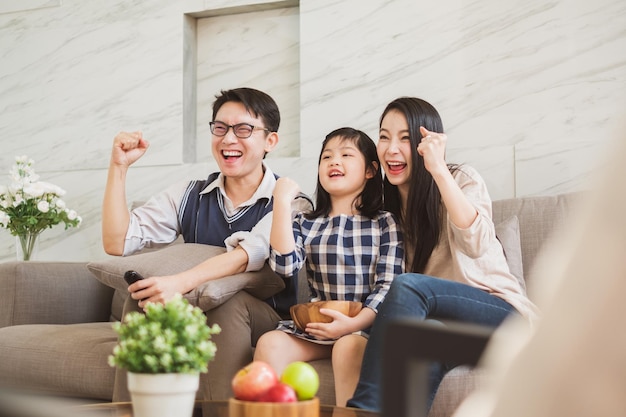 家のソファに座ってテレビを見ている幸せな家族