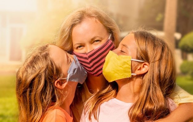 Счастливая семья, носить маски для лица. Девочки в масках целуют счастливую маму.