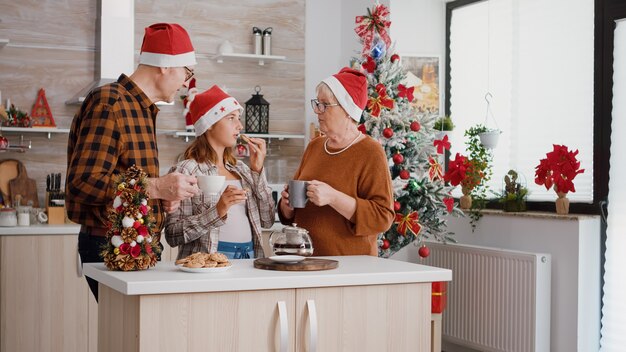 焼きたてのチョコレートクッキーを食べるクリスマスの休日を祝うサンタの帽子をかぶって幸せな家族