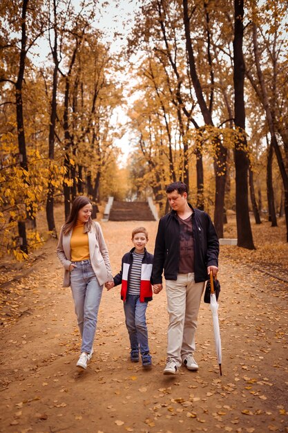 La famiglia felice con un bambino durante una passeggiata autunnale nel parco cittadino cammina lungo il vicolo divertimento in famiglia