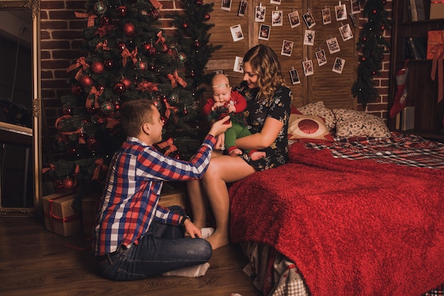 Happy family with child celebrating New Year and Christmas at decorated Christmas tree and garlands