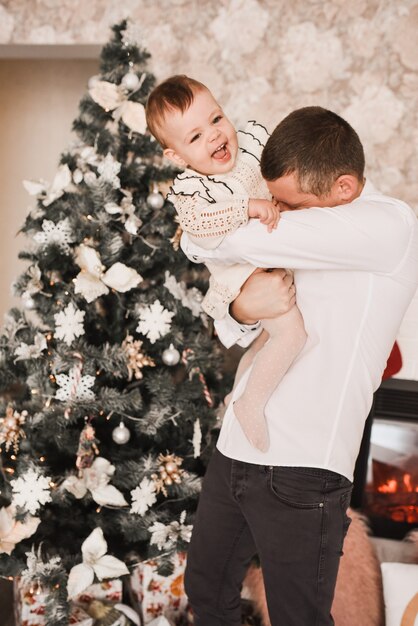 Happy family with child celebrating New Year and Christmas at decorated Christmas tree and garlands