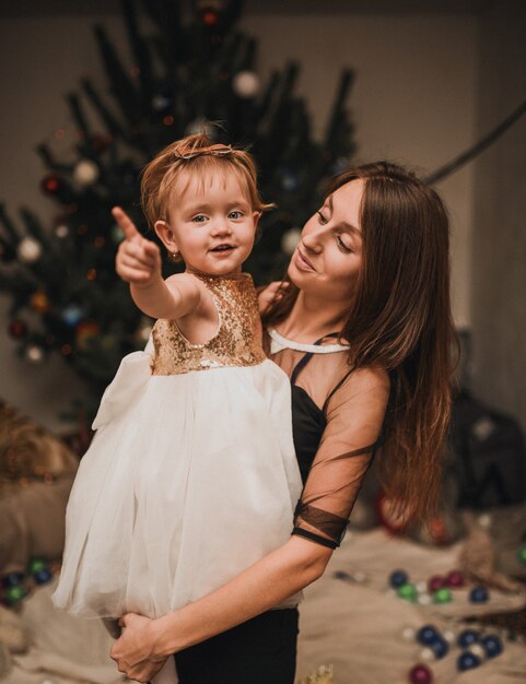 Счастливая семья с ребенком, празднующим Новый год и Рождество на украшенной елке и гирляндах