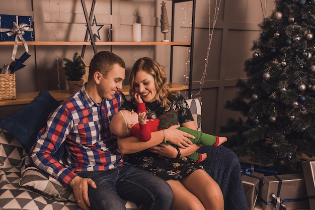 Happy family with child celebrating New Year and Christmas at decorated Christmas tree and garlands