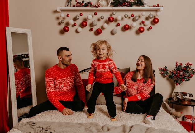 Famiglia felice con bambino che celebra il nuovo anno e il natale all'albero di natale decorato e alle ghirlande