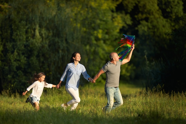 Happy family with child girl launches multicolor kite in sunny summer day. Carefree time