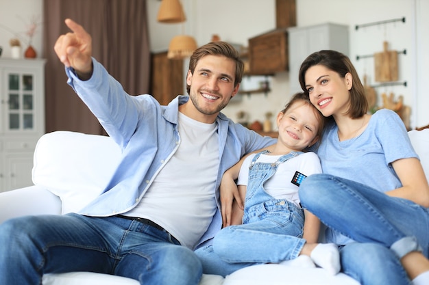 Famiglia felice con bambino seduto sul divano a guardare la tv, giovani genitori che abbracciano la figlia che si rilassano insieme sul divano.