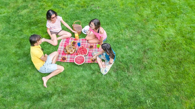 Happy family with children having picnic in park, parents with kids sitting on garden grass and eating healthy meals outdoors