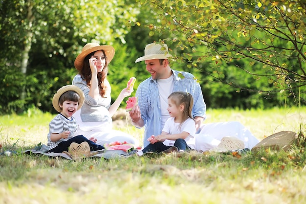 Happy family with children having picnic in park parents with kids sitting on garden grass and eating watermelon outdoors