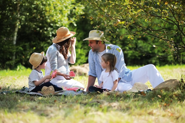 Happy family with children having picnic in park parents with kids sitting on garden grass and eating watermelon outdoors