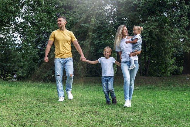 Happy family with children in the park on a sunny day Mom dad and little daughter and son in jeans and white tshirts laugh and hug Love and tenderness