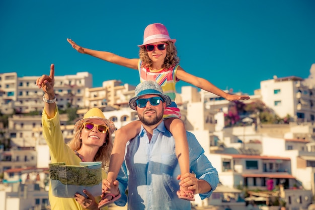 Happy family with colorful sunglasses and hats holding a map with an european town in the background