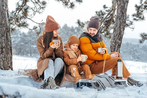 Happy family with cups of hot tea spending time together in winter forest