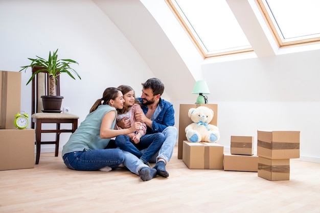 Happy family with daughter sitting on the parquet floor and celebrating moving into new house real estate