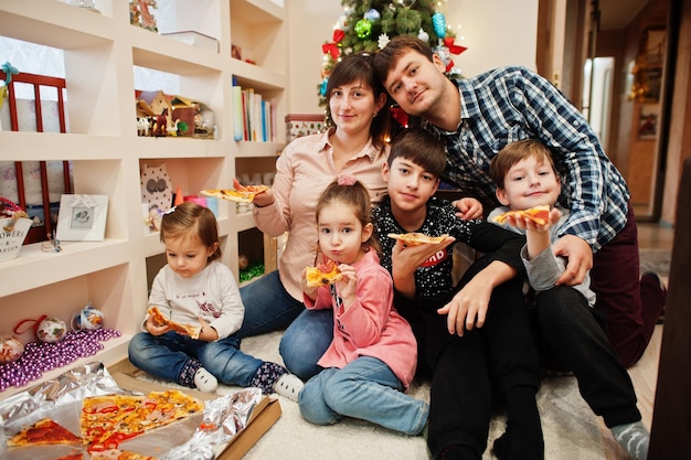 Happy family with four kids eating pizza at home.