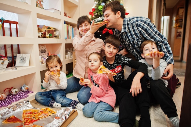 Счастливая семья с четырьмя детьми едят пиццу дома.
