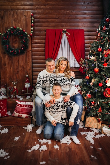 Happy family with gifts around the Christmas tree and fireplace