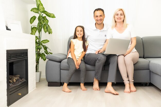 Happy family with kid girl having fun using laptop together\
sitting on sofa, parents and child daughter laughing relaxing at\
home with computer watching funny internet video, making online\
call