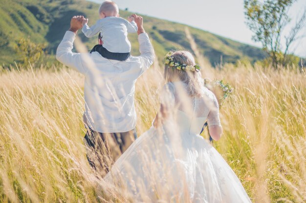 Happy family with kid walking together in wheat field on warm and sunny summer day. Soft focus.