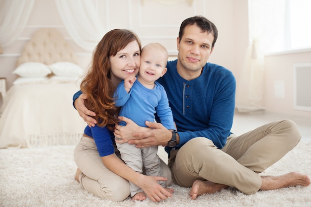 Famiglia felice con il piccolo bambino che gioca sul tappeto