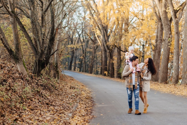 Happy family with little baby walk at park road with yellow trees at autumn