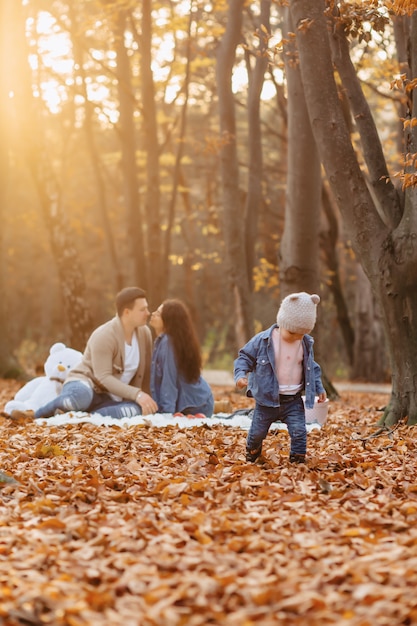 Happy family with little cute child in park on yellow leaf with big pumpkin in autumn