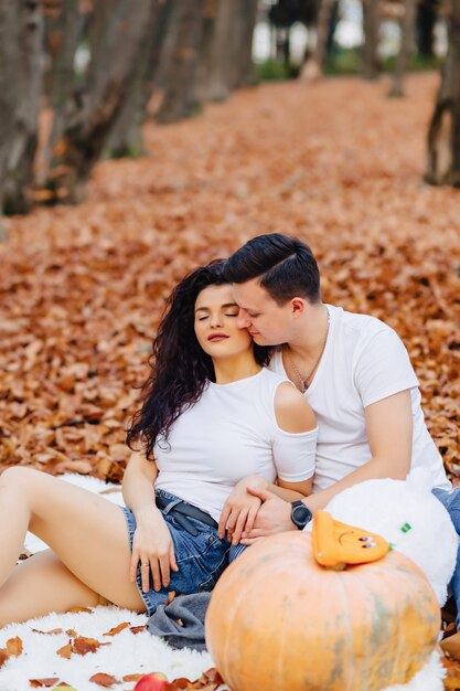 Happy family with little cute child in park on yellow leaf with big pumpkin in autumn