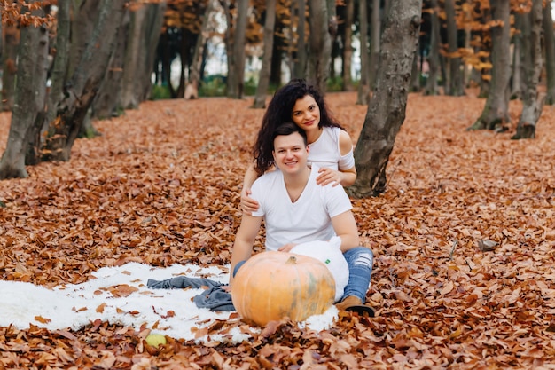 Happy family with little cute child in park on yellow leaf with big pumpkin in autumn