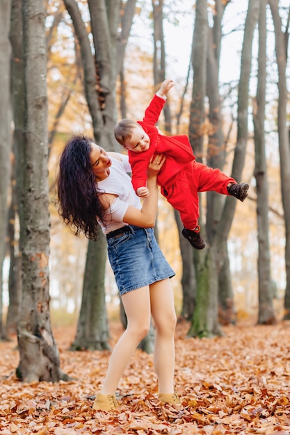 Happy family with little cute child in park on yellow leaf with big pumpkin in autumn