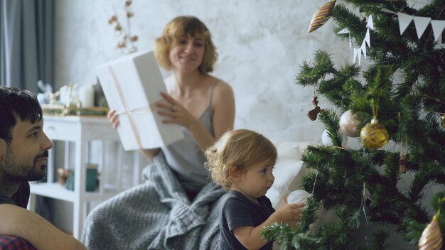 家でクリスマスツリーを飾る小さな娘と幸せな家族