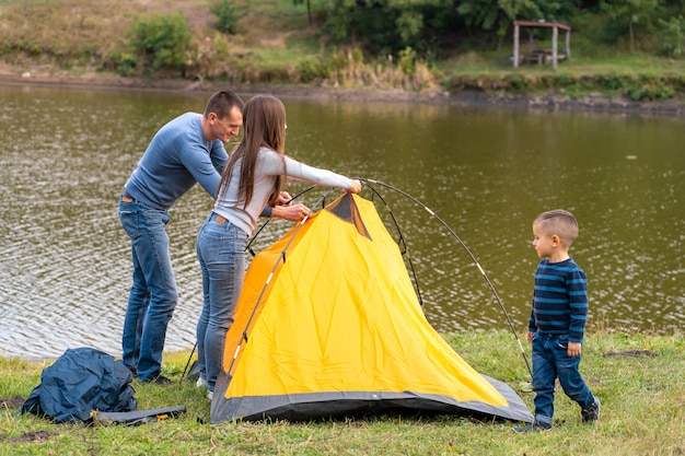 Happy family with little son set up camping tent. Happy childhood, camping trip with parents. A child helps to set up a tent