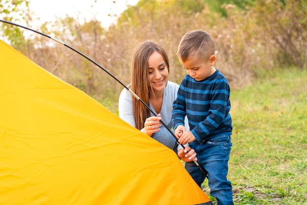 작은 아들과 함께 행복 한 가족 캠핑 텐트를 설정합니다. 행복한 어린 시절, 부모와 함께 캠핑 여행. 아이가 텐트를 세우는 데 도움