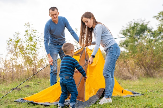 Happy family with little son set up camping tent. Happy childhood, camping trip with parents. A child helps to set up a tent