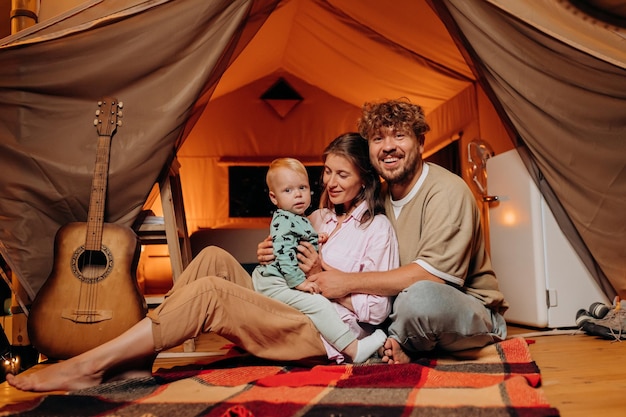 Happy family with lovely baby playing and spend time together in glamping on summer evening Luxury camping tent for outdoor recreation and recreation Lifestyle concept