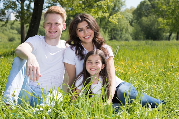 Famiglia felice con uomo, donna e bambino seduti sull'erba nel parco cittadino