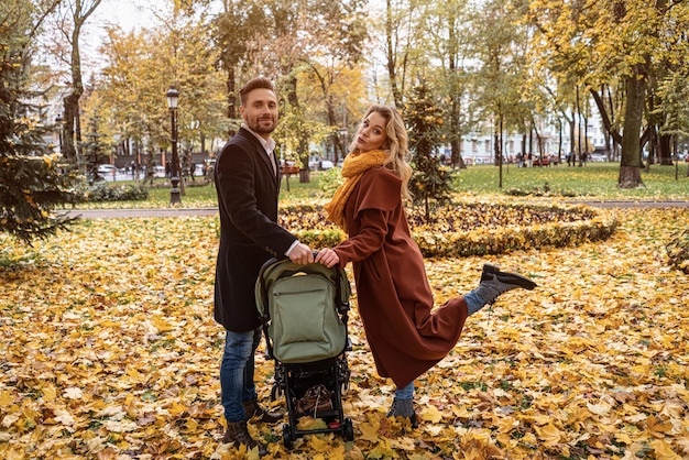 Happy family with a newborn baby in a stroller walking in an autumn park happy mother posing holding...