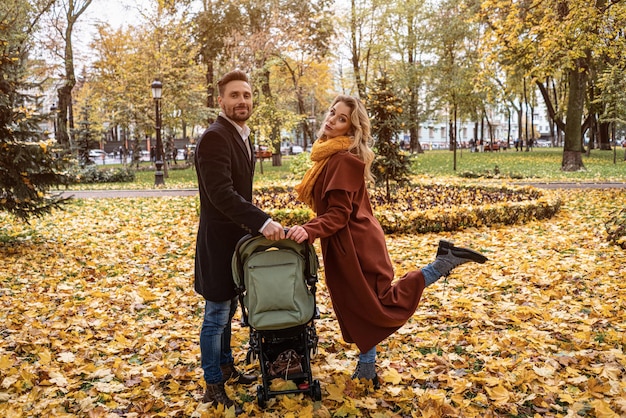 Famiglia felice con un neonato in un passeggino che cammina in un parco autunnale madre felice in posa tenendo...