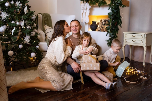 Foto famiglia felice con regali in camera genitori e bambini piccoli che si divertono sul pavimento di casa vicino all'albero all'interno