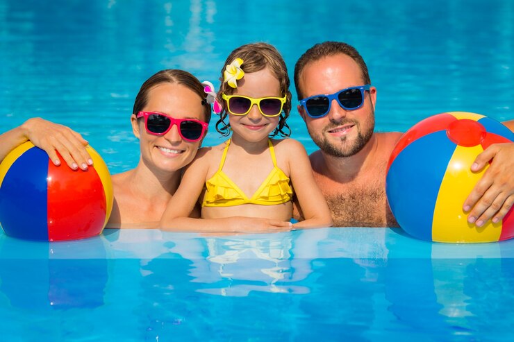 Photo happy family  with sunglasses and flowers on their hair with inflatable balls inside the pool