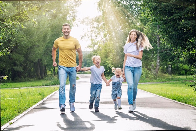 Happy family with two children joyfully run in the park on a sunny summer day Parents son and daughter in jeans and Tshirts Love tenderness and relationships in the family