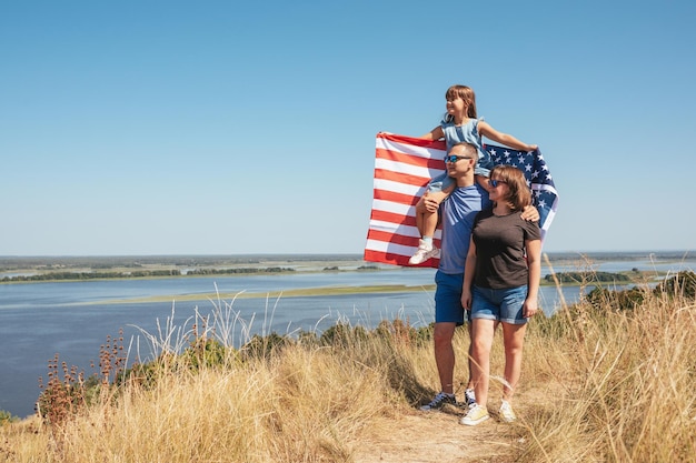 日当たりの良い夏の日に自然の中で米国旗と幸せな家族